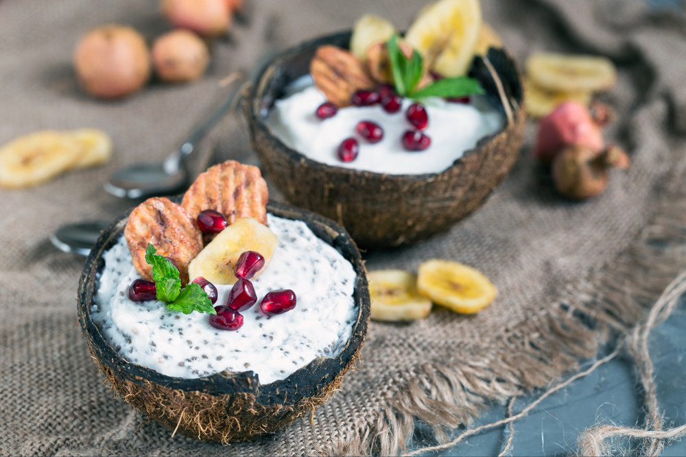 Coconut vegan yogurt served in coconut with banana chips, pomegranate and chia seeds
